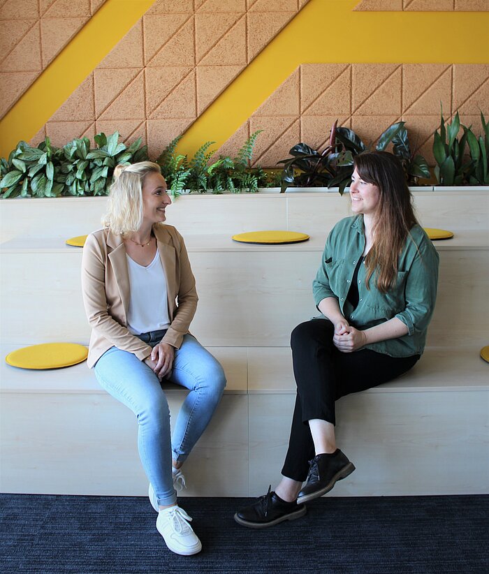 Two smiling women sitting together in a modern office setting.