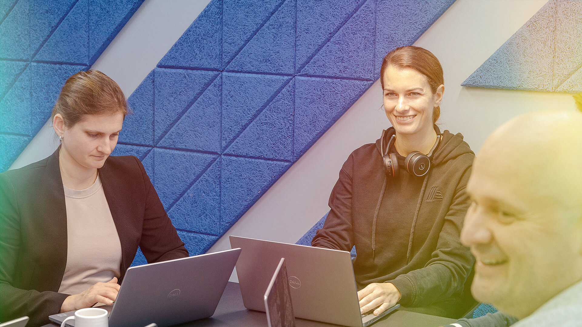 Drei Personen sitzen an einem Tisch mit Laptops und arbeiten zusammen.