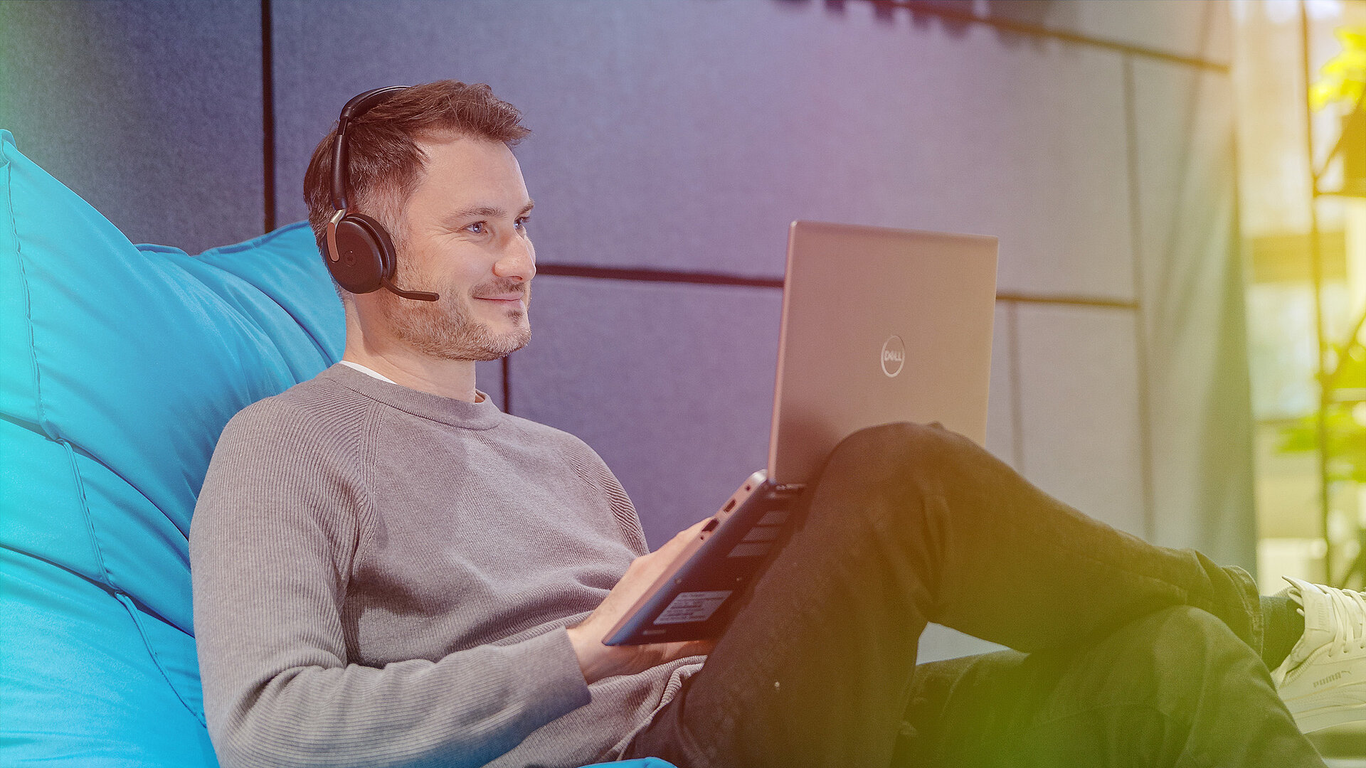 Ein Mann mit Kopfhörern sitzt auf einem Sitzsack und arbeitet an einem Laptop.