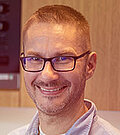 A smiling man with glasses and in a blue shirt.