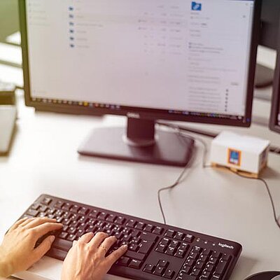Eine Frau tippt auf einer Tastatur vor zwei Computermonitoren.
