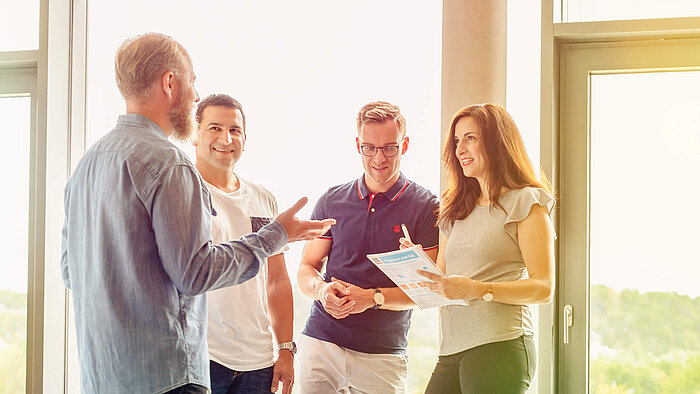 A group of people standing in an office and talking.