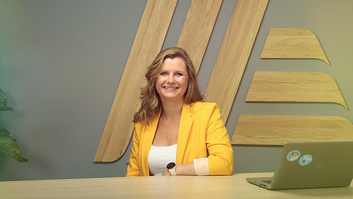 A woman in a yellow top sitting at a desk with a laptop.