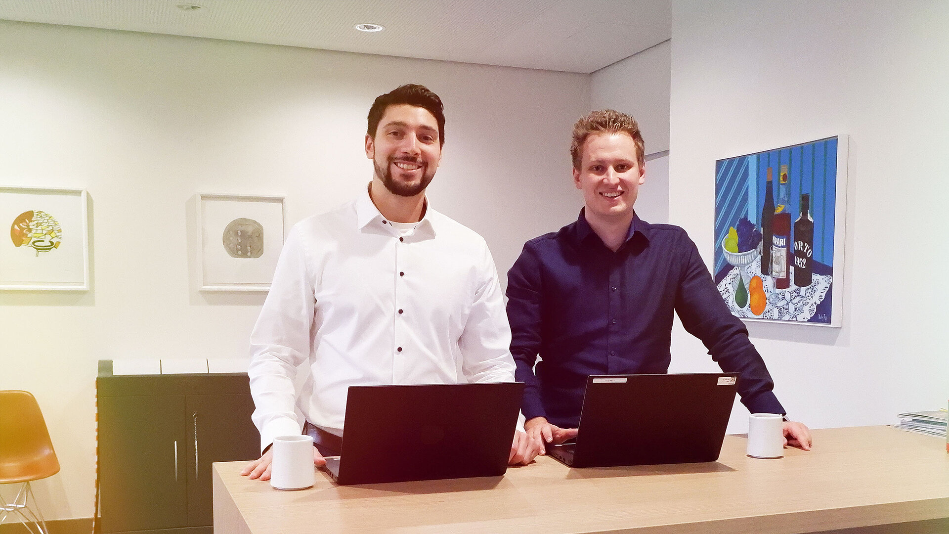 Zwei Männer stehen an einem Schreibtisch mit Laptops.