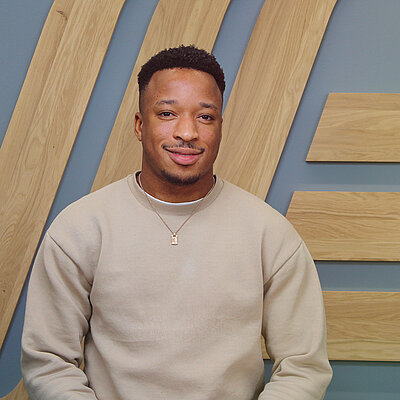 Ein Mann in einem Pullover sitzt vor einer Wand.