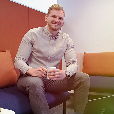 Ein lächelnder Mann sitzt auf einem Sofa mit einem Laptop und einer Tasse Kaffee.