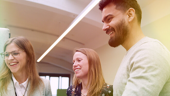 Three smiling people looking at a computer screen.
