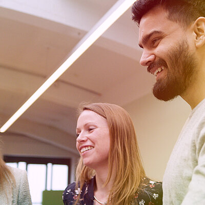 Drei lächelnde Personen schauen auf einen Computerbildschirm.