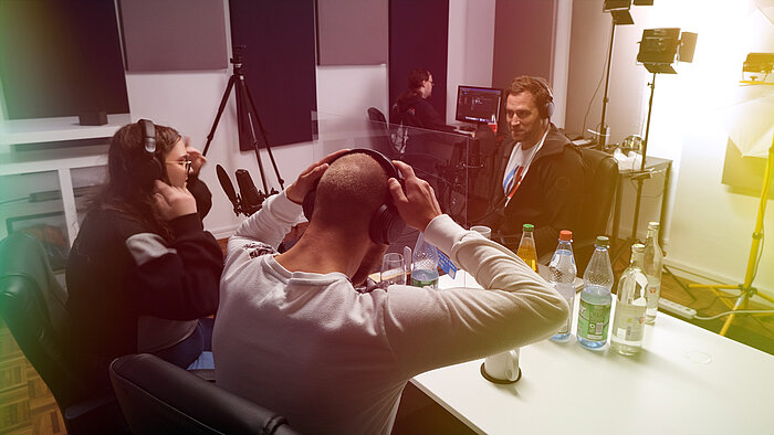Three people with headphones talking at a table.