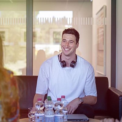 Drei Personen mit Kopfhörern unterhalten sich an einem Tisch.