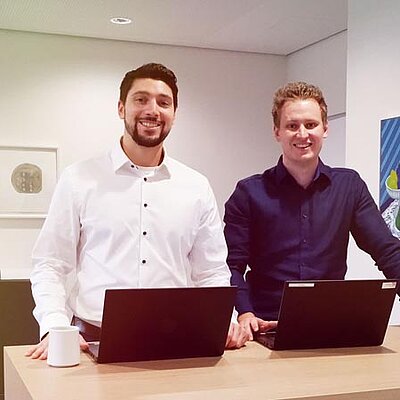 Zwei Männer stehen an einem Schreibtisch mit Laptops.