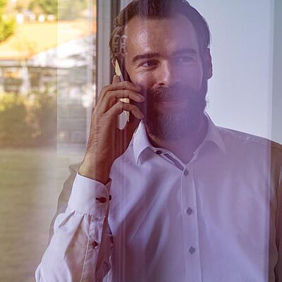 Ein Mann mit einem Handy steht vor einem Fenster und telefoniert.