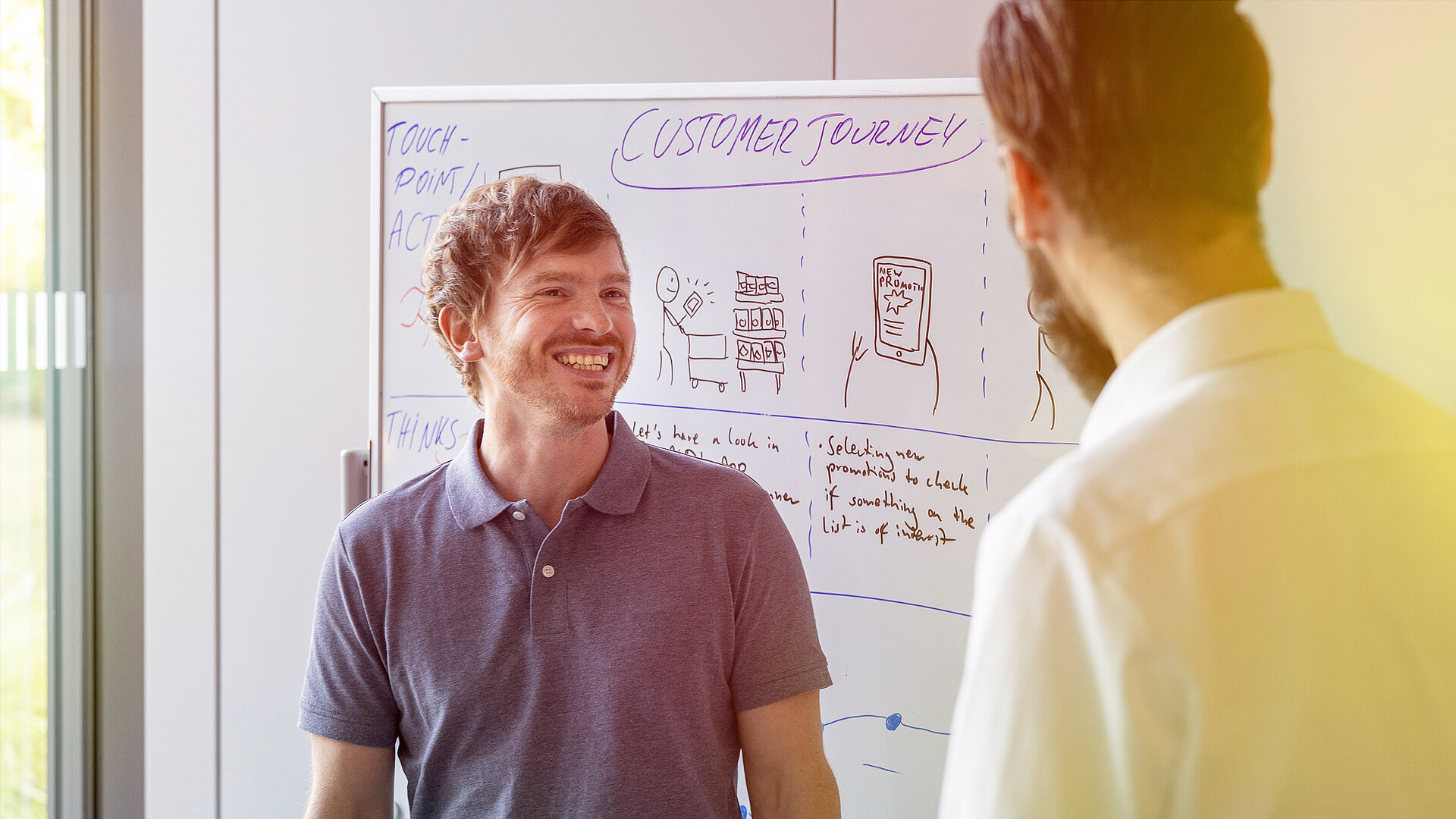 Two men talking in front of a board.