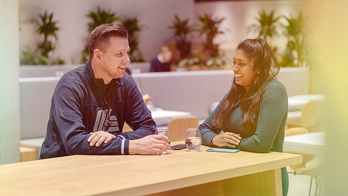 A man and a woman sitting at a table in the canteen and talking.
