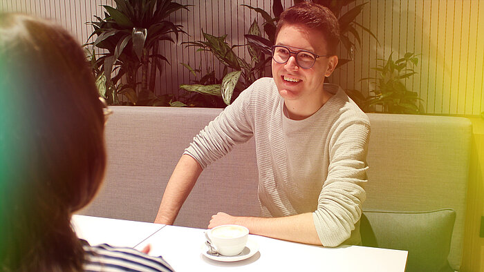 A man and a woman sitting at a table with a cup of coffee.