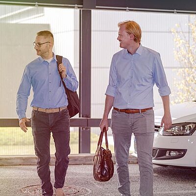 Drei Personen gehen vor einem Auto.