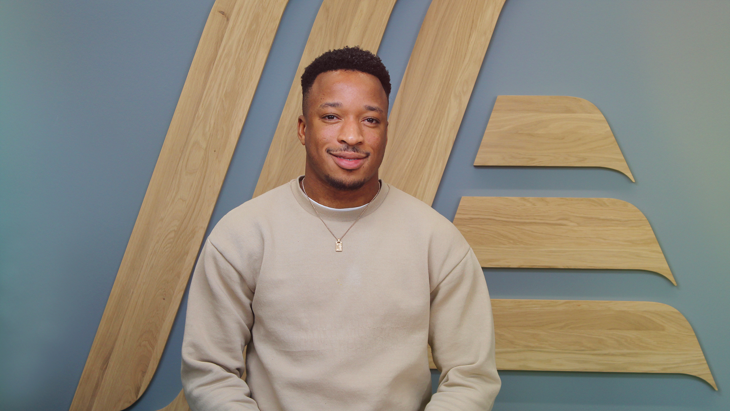 A man in a jumper sitting in front of a wall.