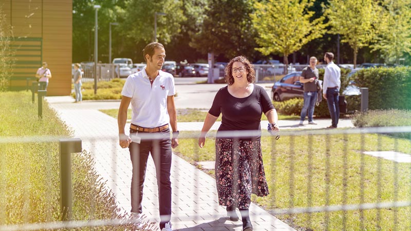 Two people walking along a path near a fence.