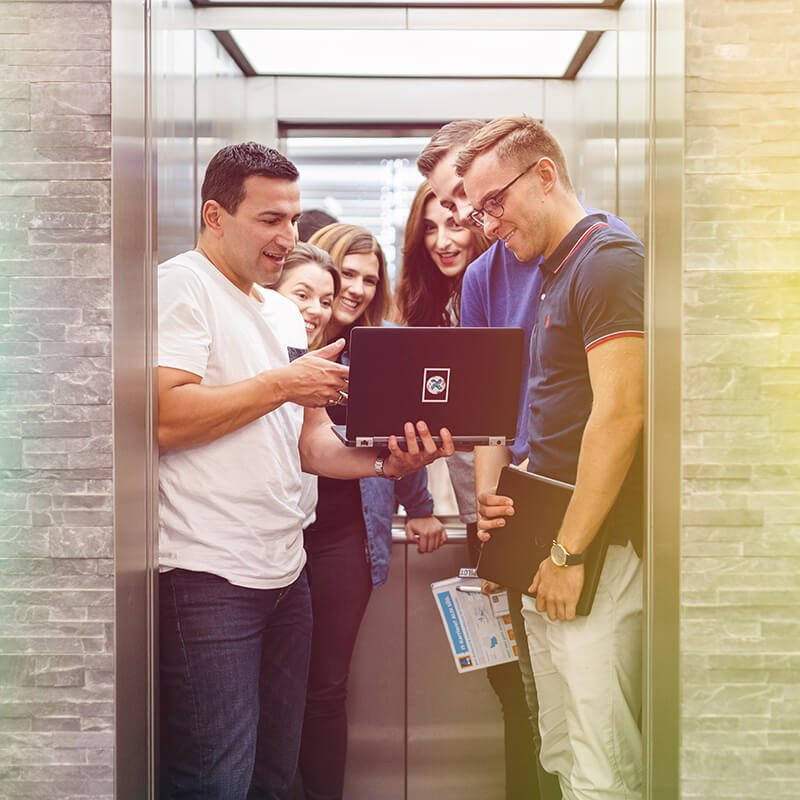 A group of people standing in a lift with a laptop.
