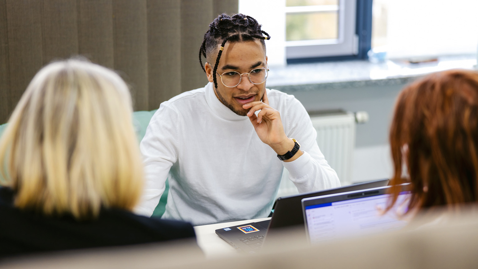 Ein Mann und zwei Frauen sitzen an einem Tisch mit einem Laptop.