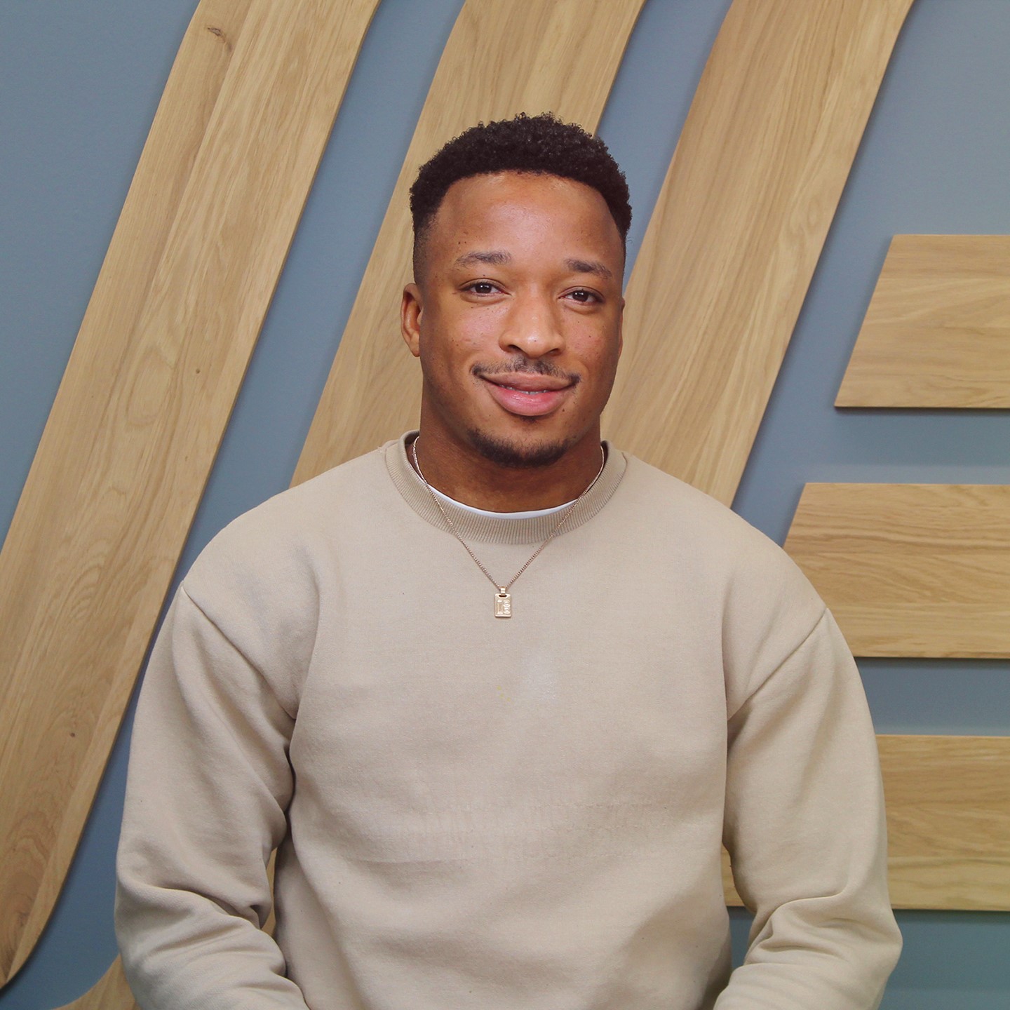 A man in a jumper sitting in front of a wall.