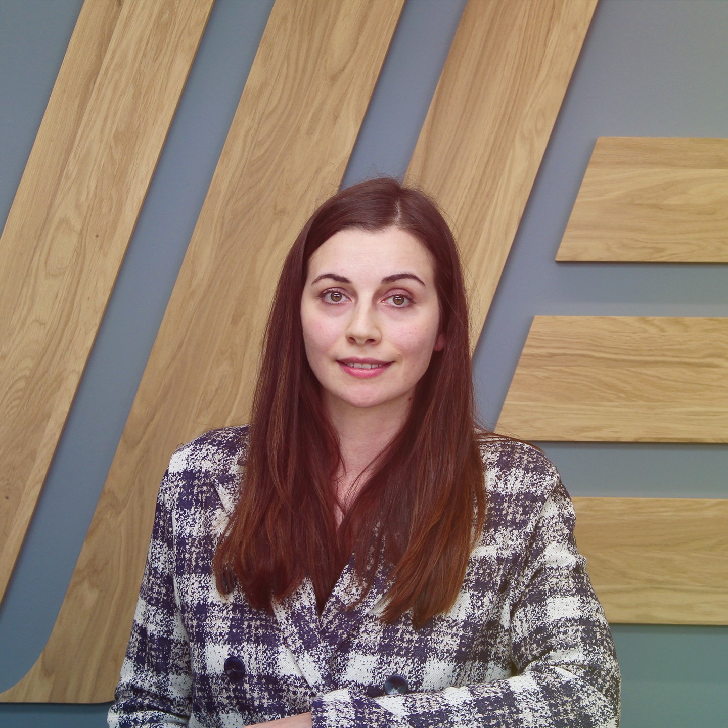 Smiling woman in a chequered shirt and jacket standing in front of a wall.