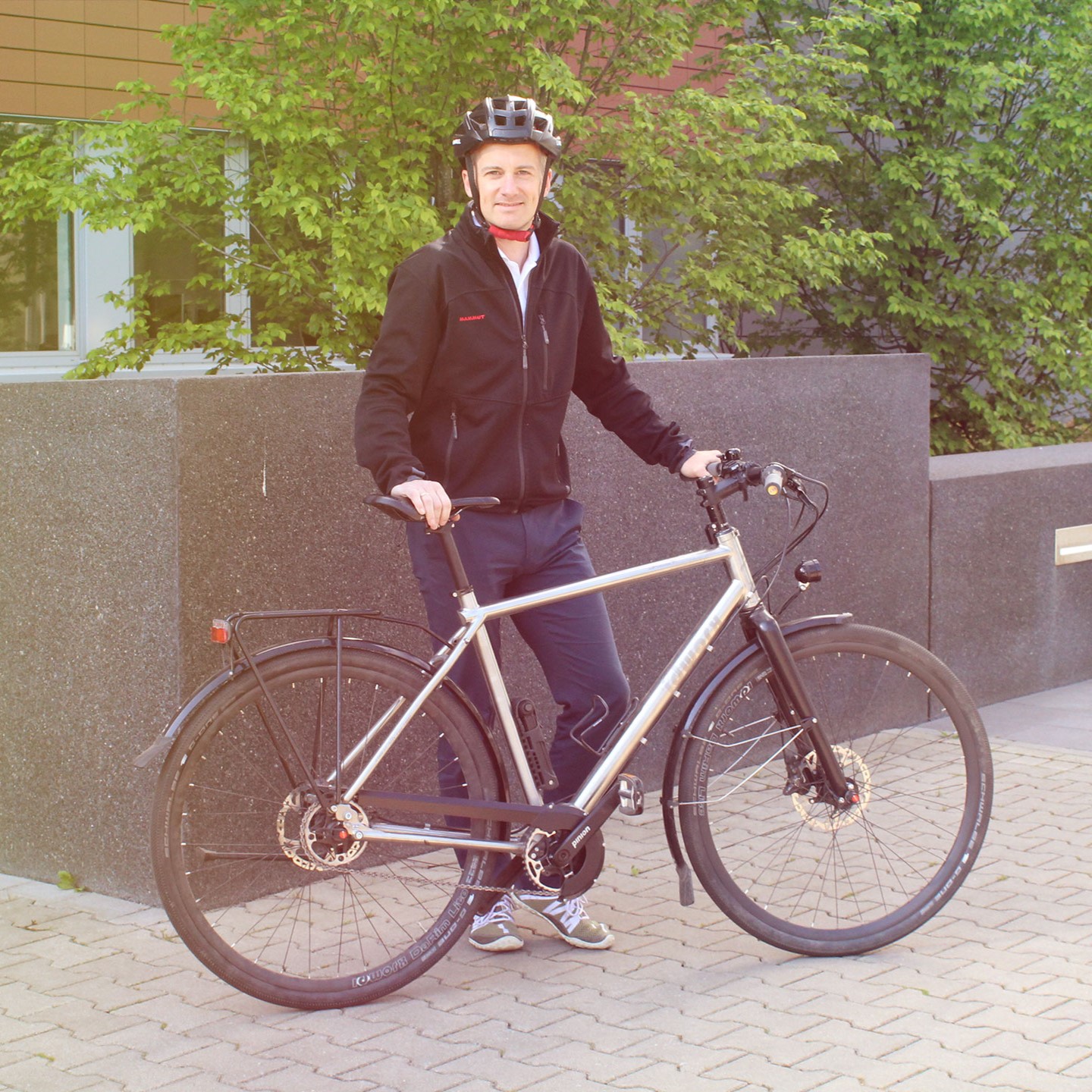 A man with a bicycle helmet standing behind a bicycle.
